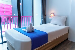 Ein Hotelzimmer mit einem Bett, einer blauen Decke, einem weißen Kopfkissen, einer Wandleuchte und einem Balkon mit rosafarbenen Geländern.
