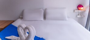 Un letto rifatto con lenzuola bianche, un cuscino blu e una coppia di asciugamani bianchi.