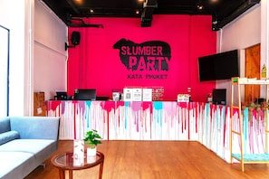 A reception area with a red wall, a counter, a sofa, a coffee table, and a TV. - Slumber Party Surf Kata (Karon)