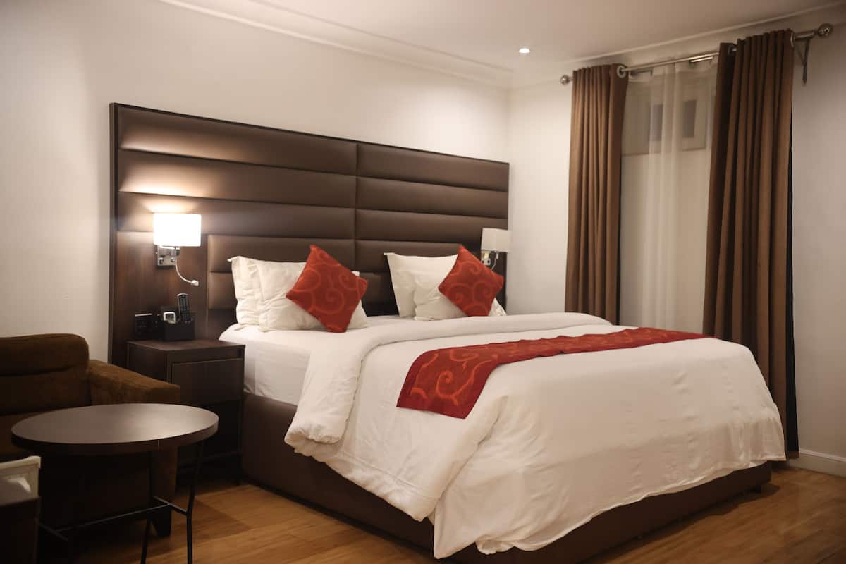 Ein Hotelzimmer mit einem großen Bett, einem Nachttisch mit Lampe, einem kleinen runden Tisch und einem braunen Sessel.