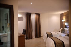 Une chambre d’hôtel avec salle de bain, deux lits, un bureau et un rideau.