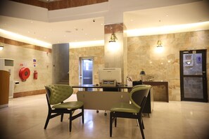 A hotel lobby with a reception desk, two green upholstered chairs, a Samsung refrigerator, and a fire extinguisher on the wall. - Bolton White Hotel - Abuja (Abuja)