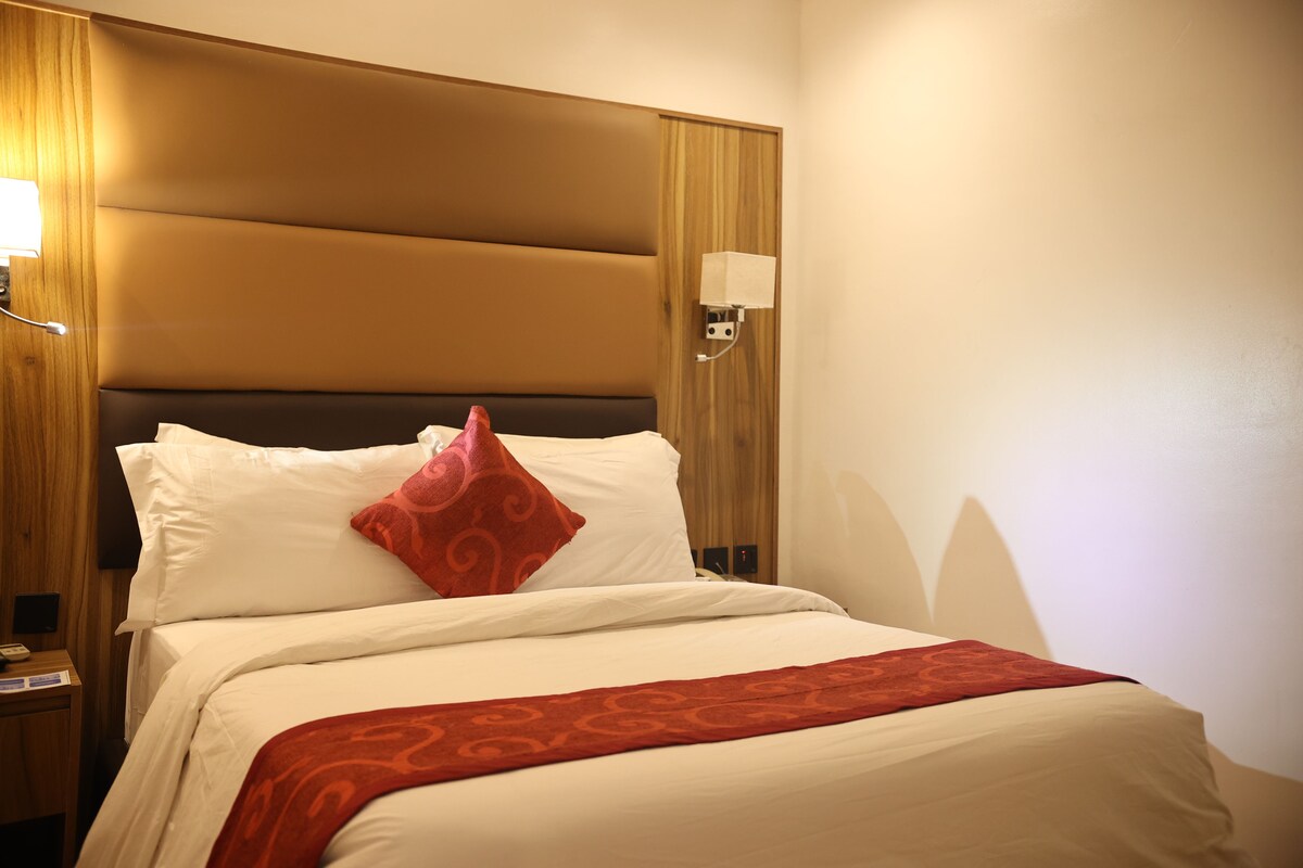 Une chambre d’hôtel avec un grand lit, une tête de lit en bois, une table de chevet avec une lampe et un luminaire fixé au mur.