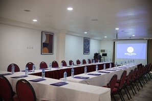 Une salle de conférence équipée de longues tables, de chaises, de bouteilles d’eau et d’un écran de projection affichant le texte « Bolton White ».