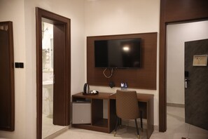 Une chambre d’hôtel avec un bureau en bois, un téléviseur fixé au mur, un petit réfrigérateur et une chaise.