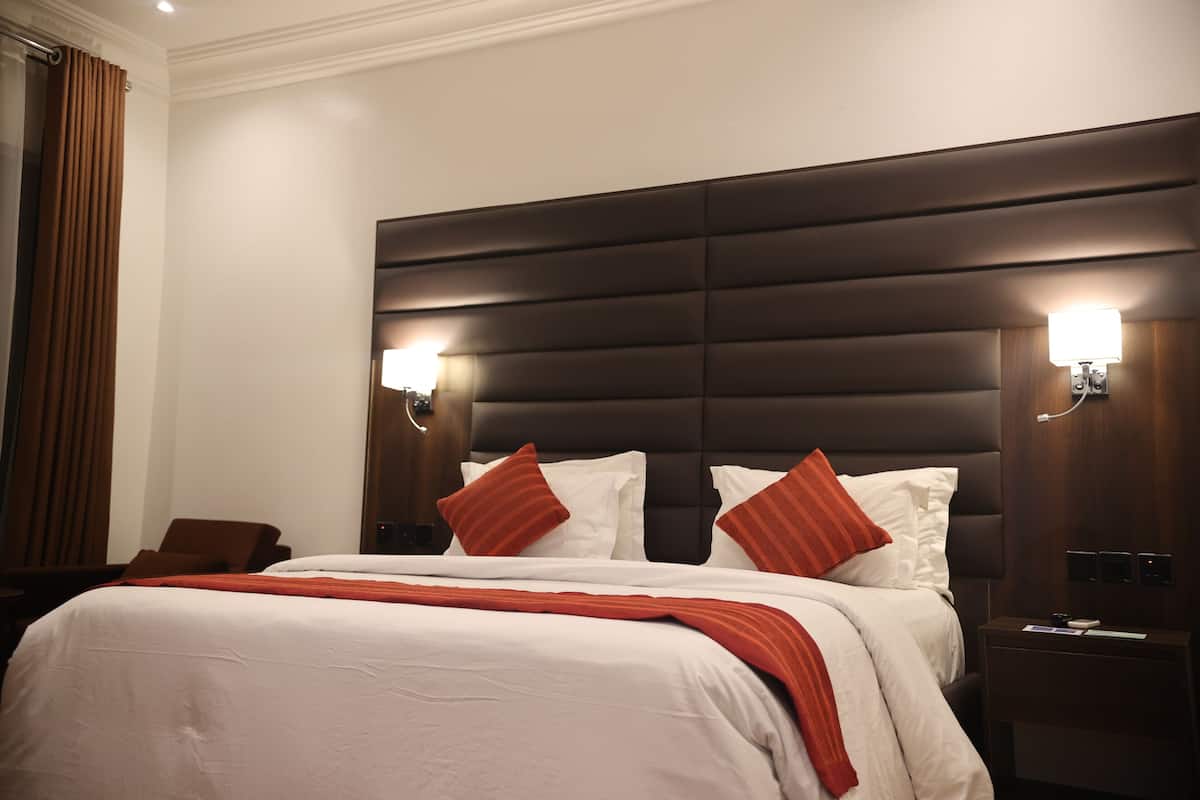 Ein Hotelzimmer mit einem großen Bett, einem dunklen Kopfteil, zwei Nachttischlampen und einem braunen Sessel.