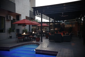 Un patio al aire libre con piscina, mesas, sillas y sombrillas.