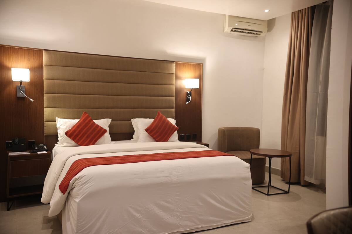 Ein Hotelzimmer mit einem großen Bett, zwei Nachttischen, einem kleinen runden Tisch und einem Sessel.