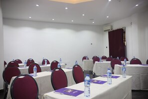 Une salle de conférence équipée de tables, de chaises, de bouteilles d’eau et d’un rideau rouge.