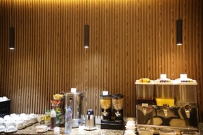 Un bar de petit-déjeuner avec divers distributeurs de nourriture et de boissons, une machine à café et un distributeur d’eau, le tout adossé à un mur en bois.