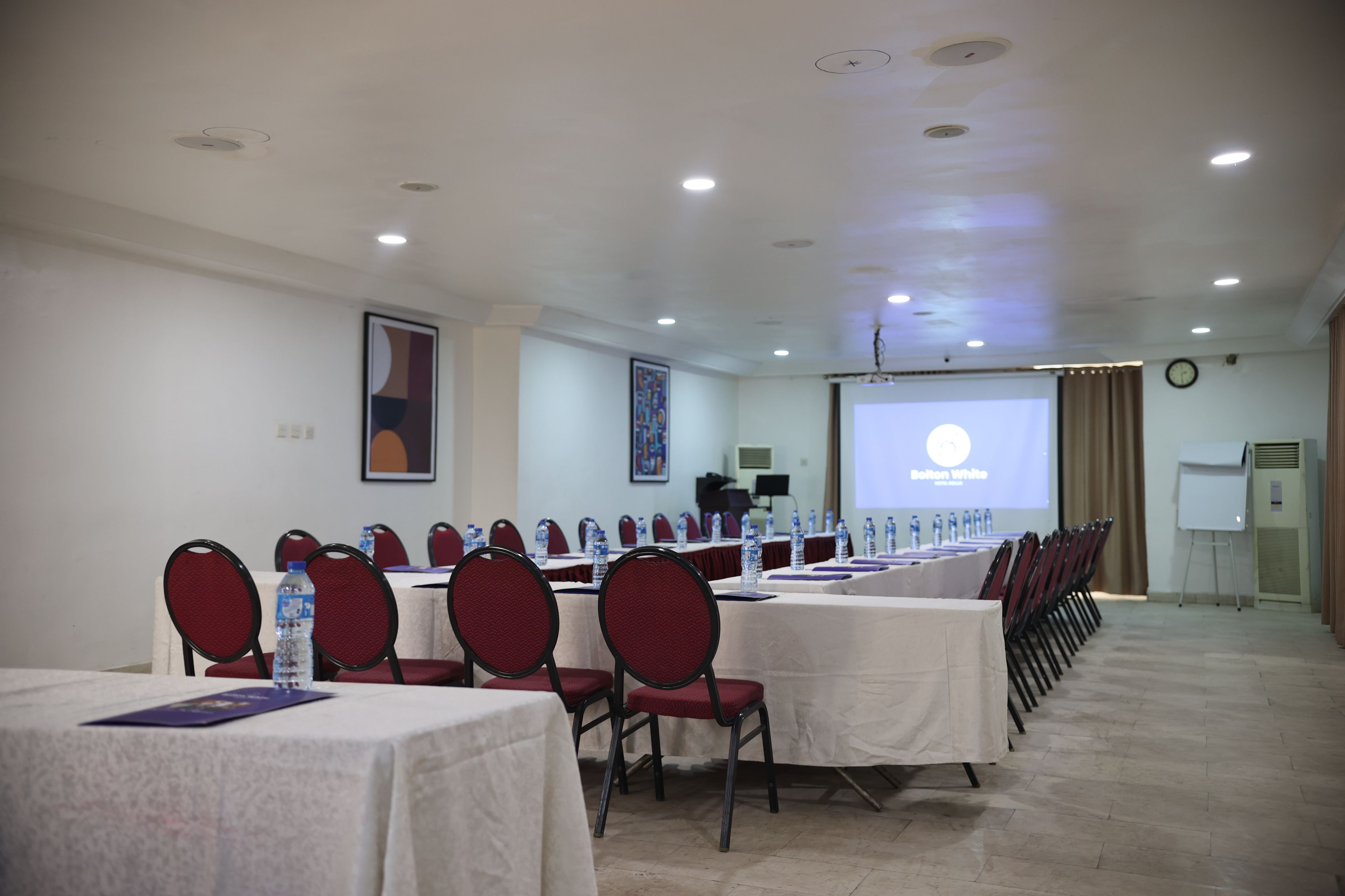 A conference room with rows of tables and chairs, a projector screen, and a whiteboard.