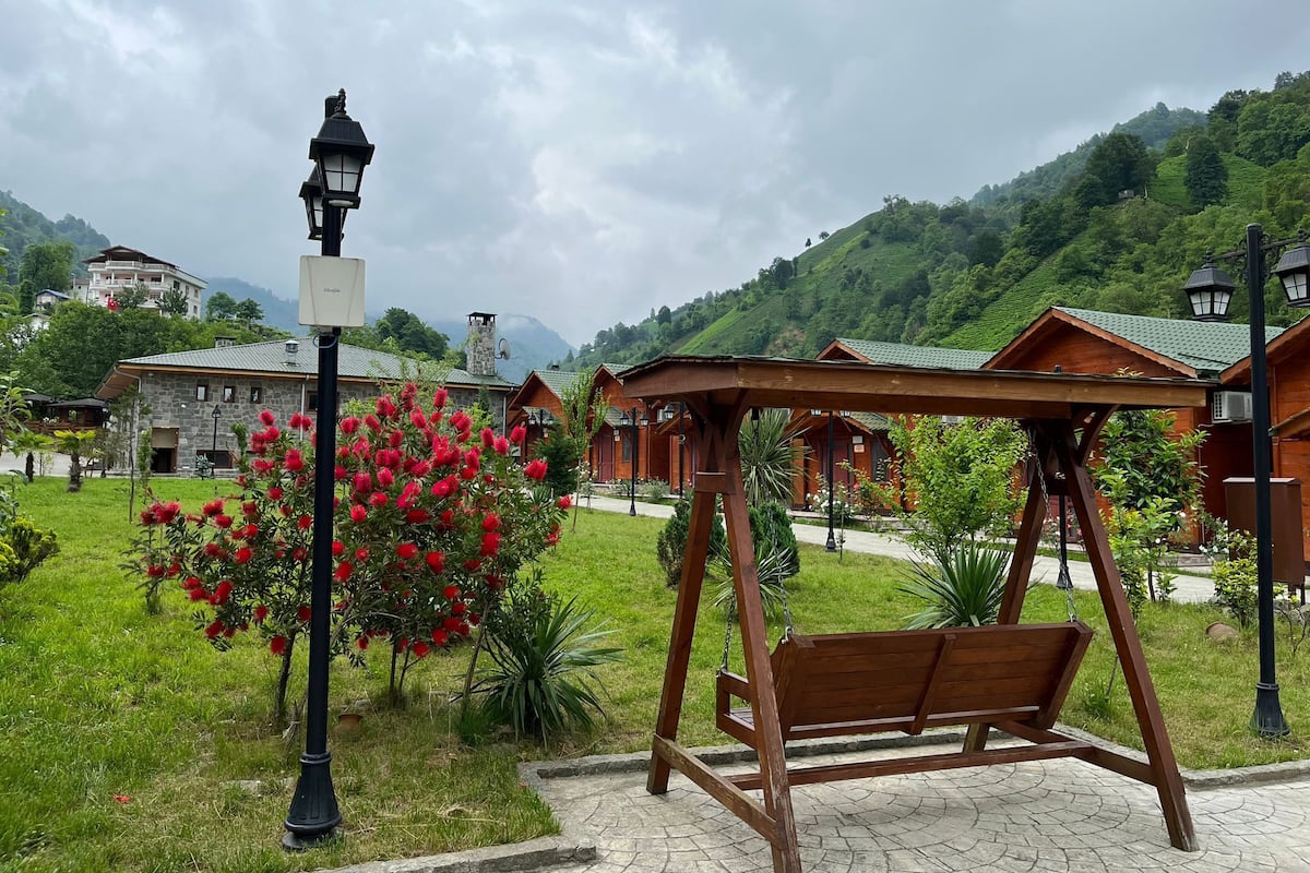Ein hölzernes Schaukelgestell in einem Garten mit einem Steinhaus im Hintergrund.