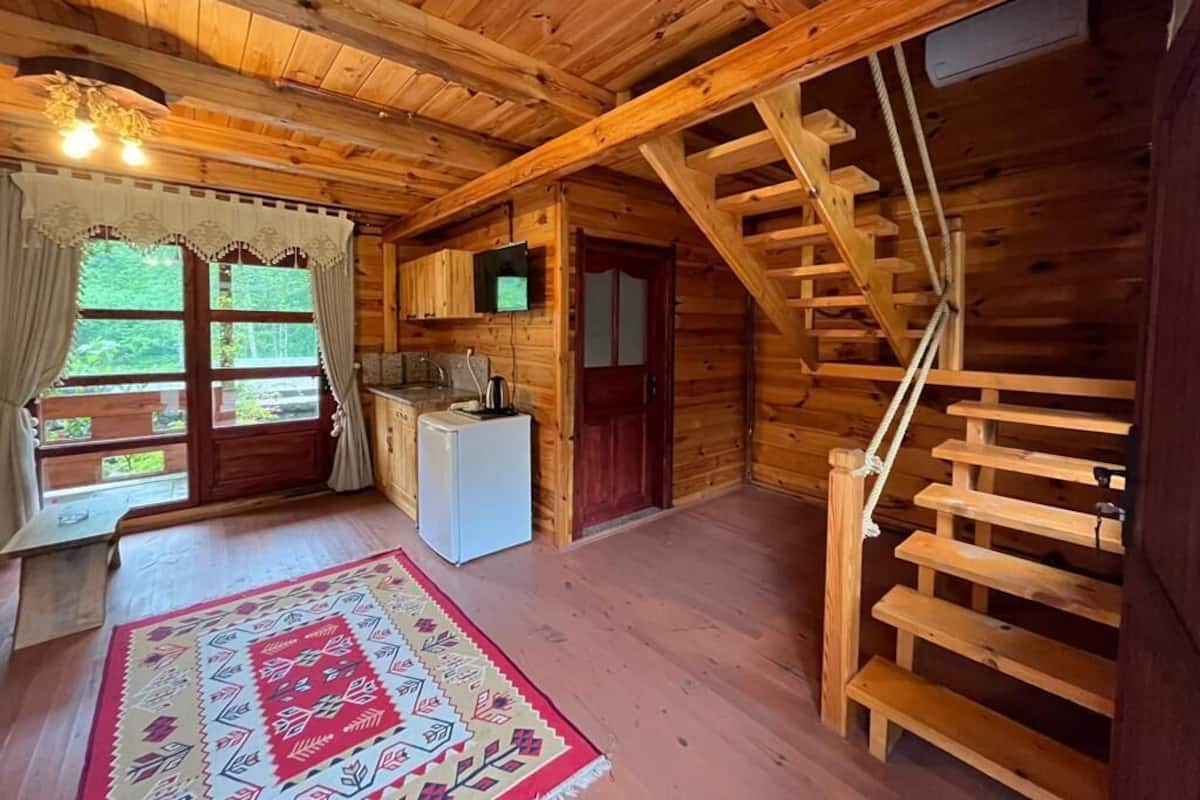 Ein Holzblockhaus-Interieur mit einer Holztreppe, einer Küchenzeile und einem großen Fenster mit Vorhängen.