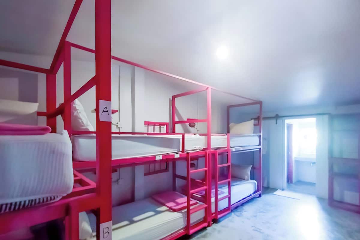 Bunk beds with pink frames and white bedding, arranged in a row with a door to the right.
