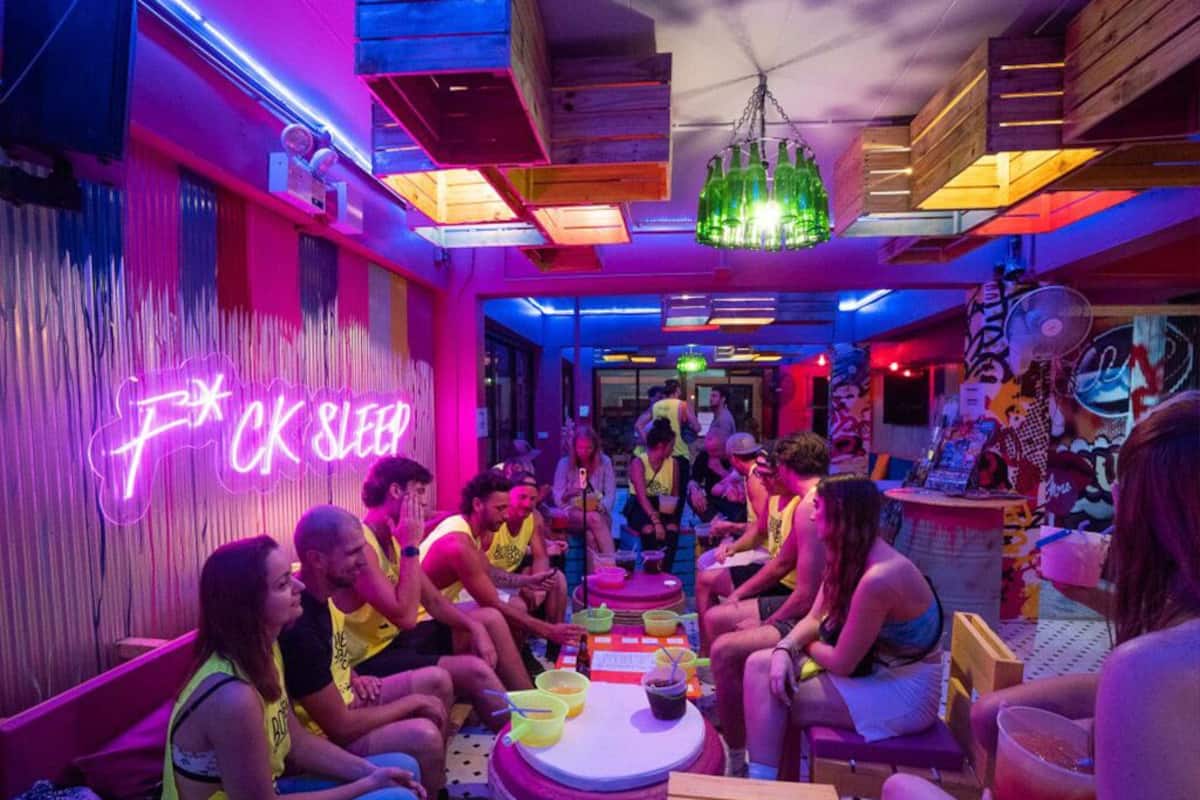 Um espaço interior vibrante com pessoas sentadas à volta de mesas, letreiros de neon e mobiliário de madeira.