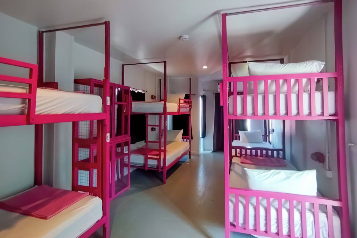 Um quarto com beliches alinhados, uma porta e uma janela.