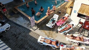 Ein Schwimmbecken mit Personen, Liegestühlen und einem Gebäude mit blauem Dach.