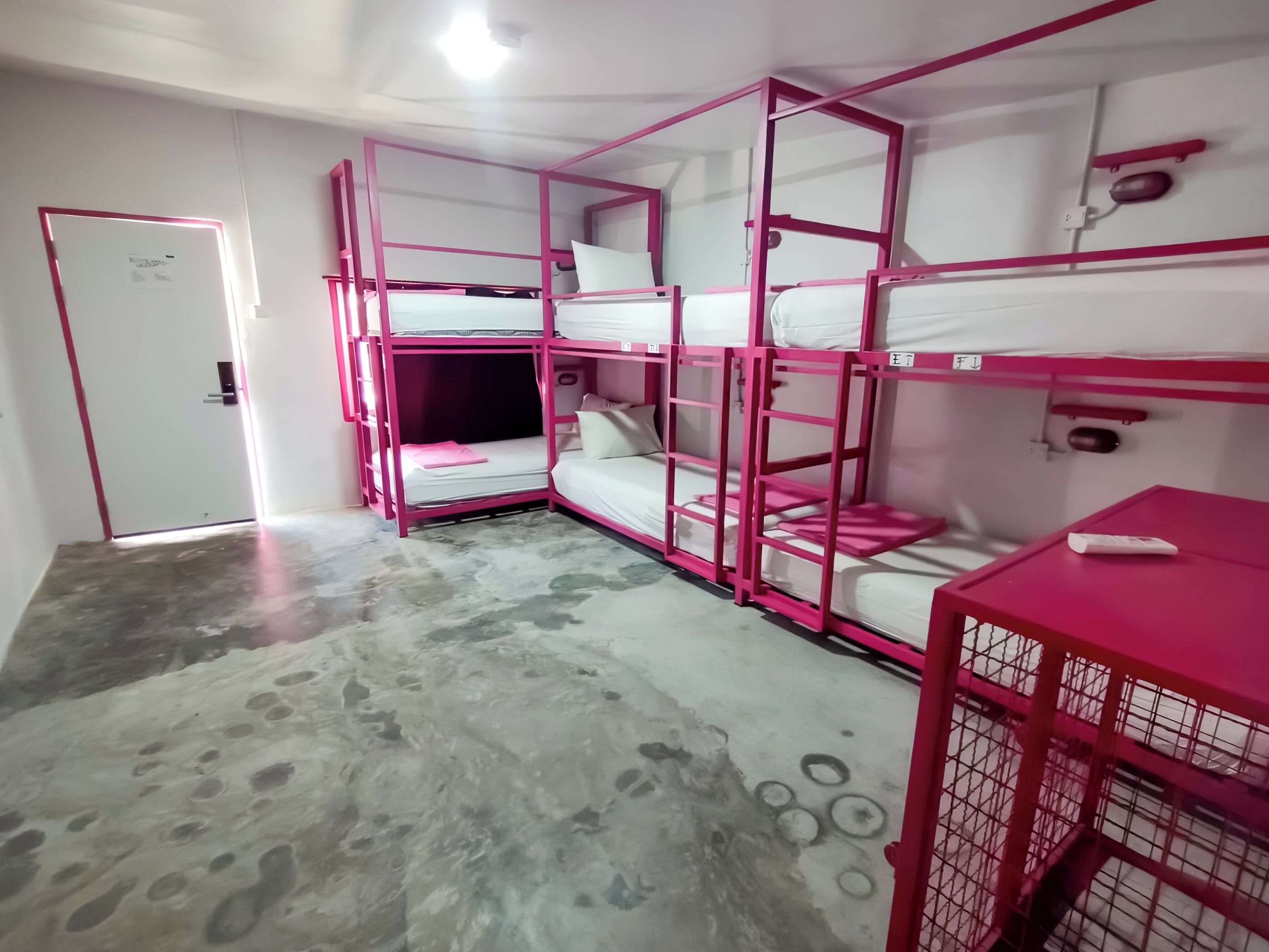 A bunk bed room with a concrete floor, a door, and a small table with a remote control.