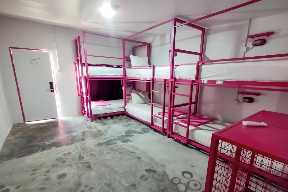Quarto com beliche, piso de concreto, uma porta e uma pequena mesa com controle remoto.