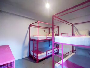 Habitación con literas de metal color rosa, una mesita pequeña y un estante en la pared.