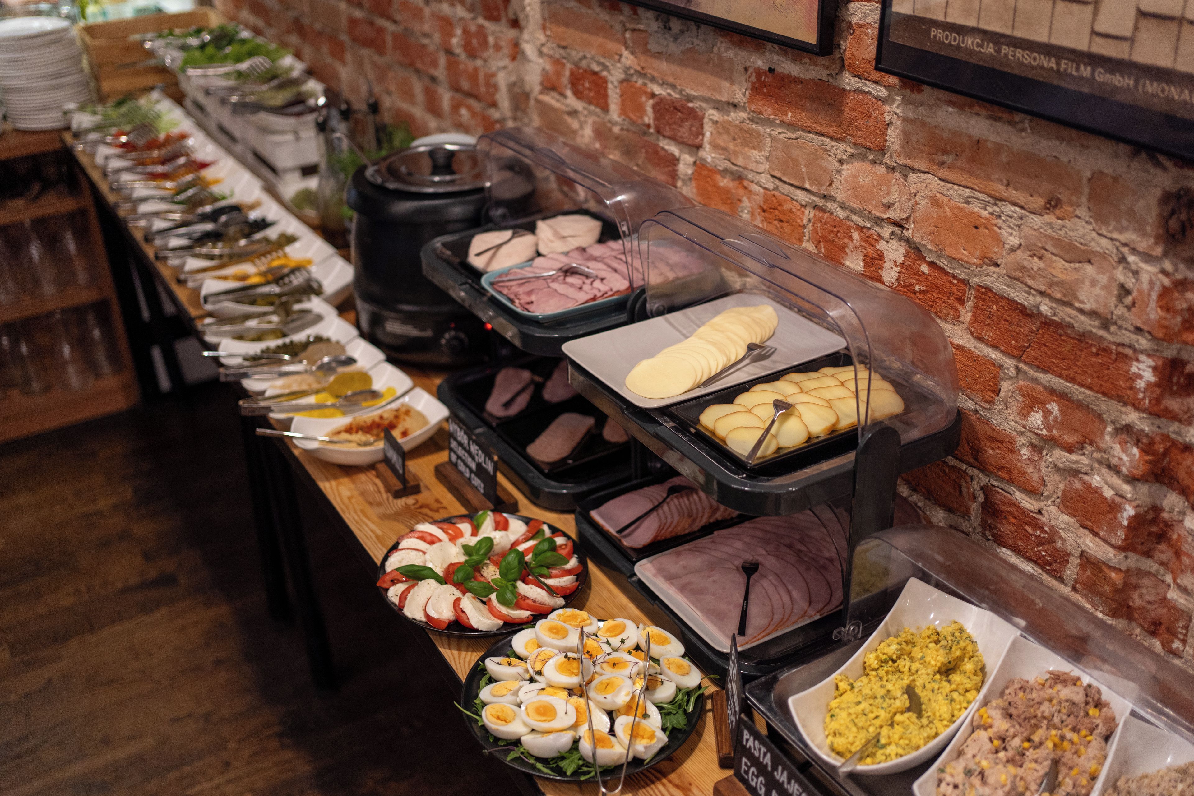 A buffet with various food options, including pasta, eggs, and meats, arranged on a wooden table against a brick wall.