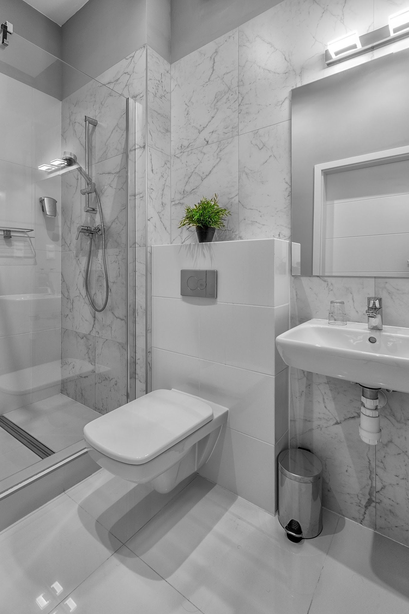 A modern bathroom with a glass-enclosed shower, a toilet, a sink, and a marble-tiled wall.