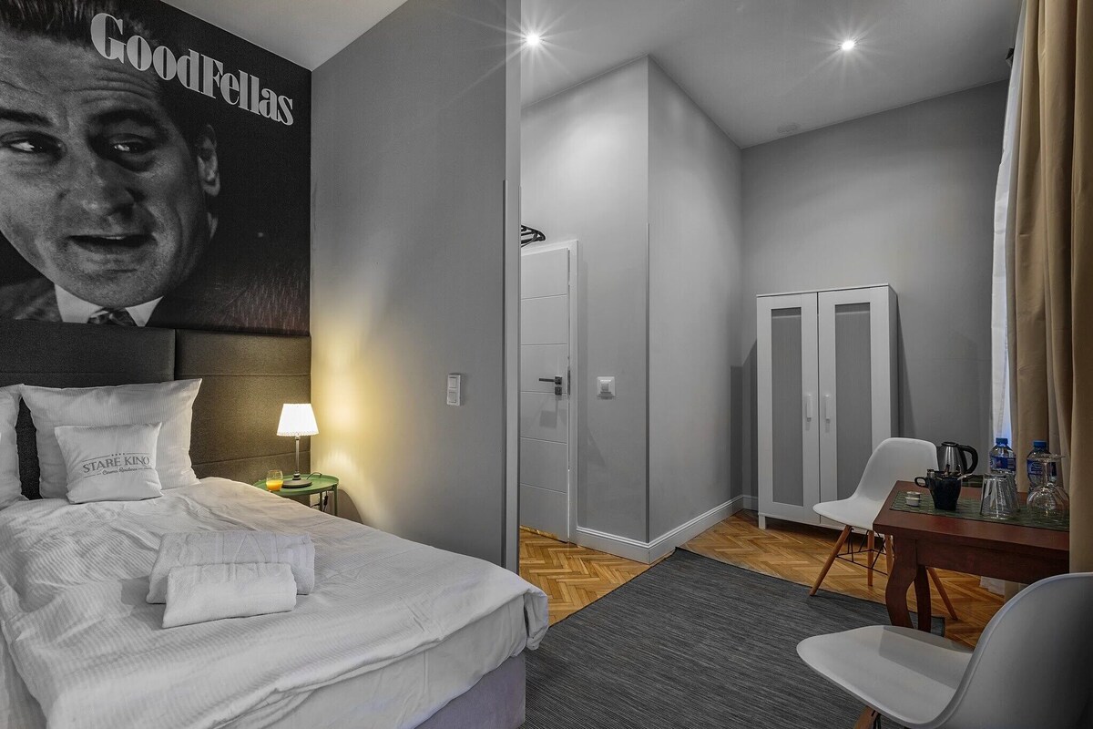 Ein Hotelzimmer mit Bett, Nachttisch mit Lampe, Schreibtisch mit Stühlen und Kleiderschrank.