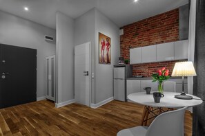 A modern kitchen with white cabinets, a brick wall, and a dining area with a table and chairs. - Cinema Rooms - Piotrkowska (Łódź)