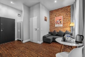 A modern room with a brick wall, a grey sofa, a round table with a kettle, and a door.