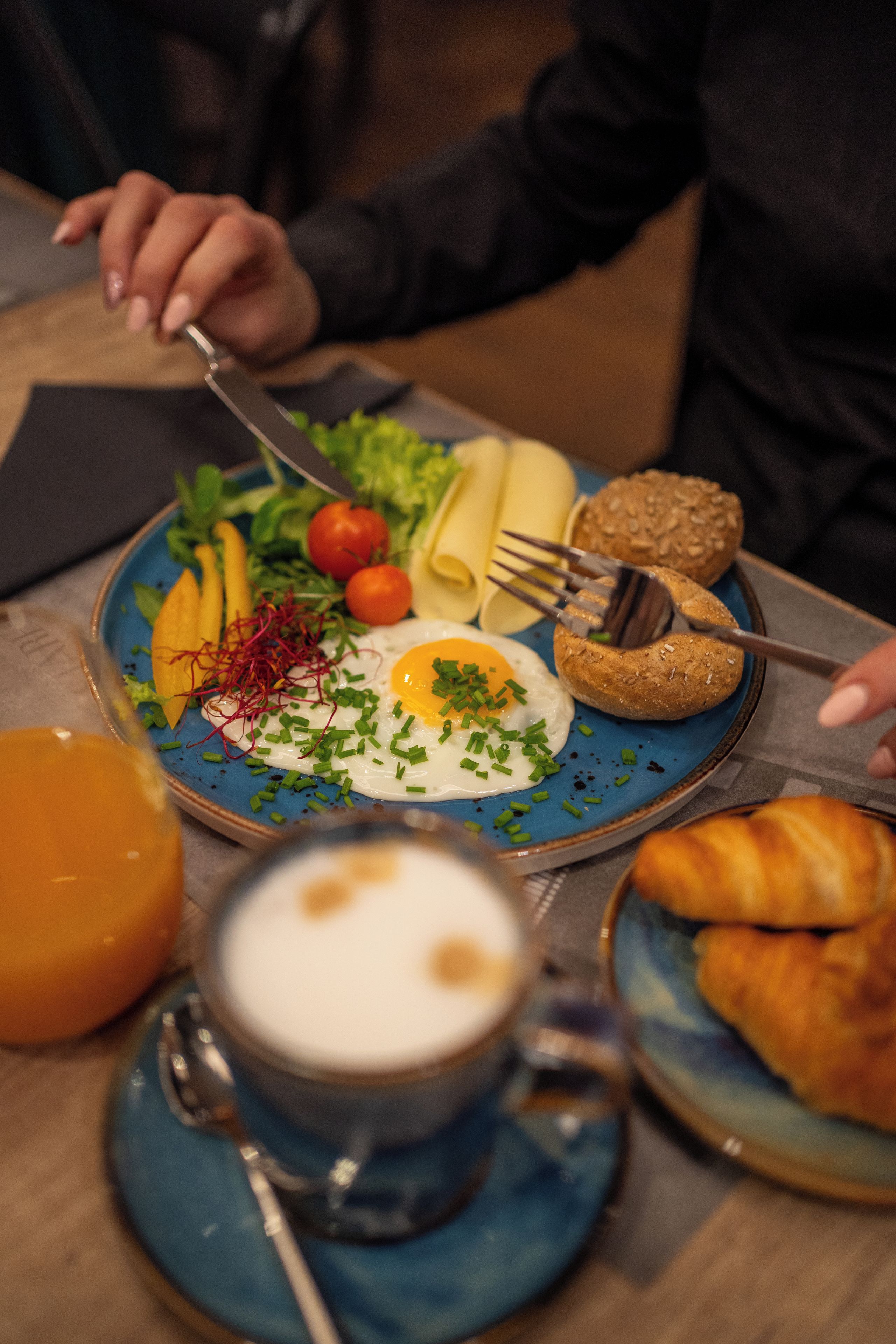 A meal with a plate of food, a cup of coffee, and a croissant on a table.