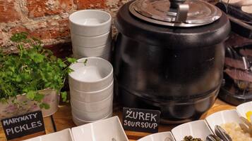A buffet setup with labeled containers for pickles and sour soup, a large black pot, and a potted plant.