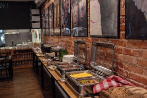 A buffet setup with various food items, a brick wall, and framed pictures.