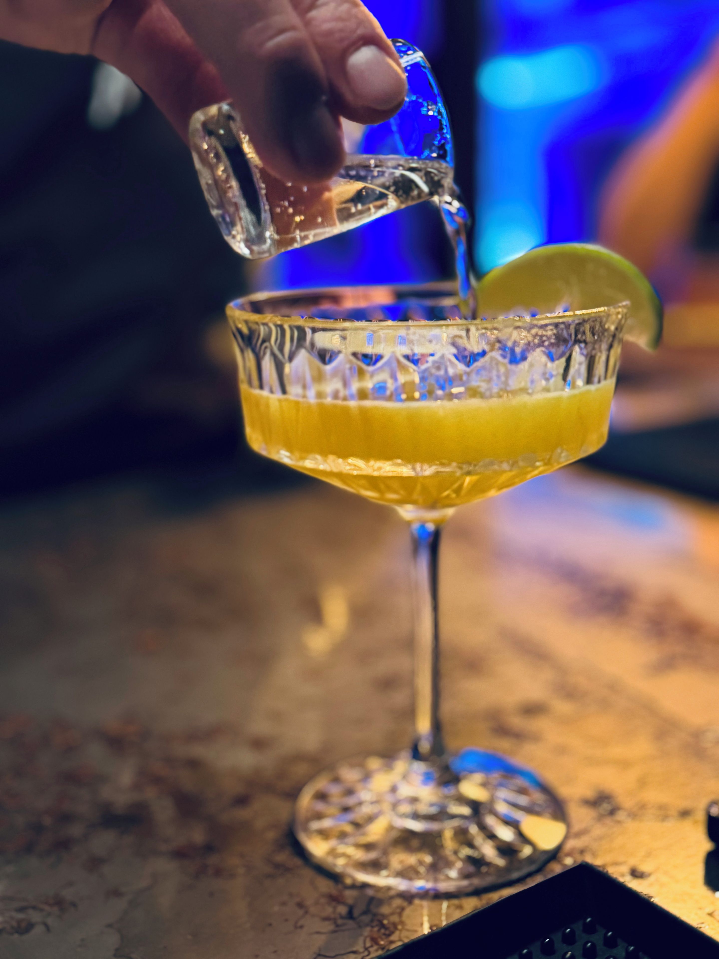 A hand pouring a clear liquid into a glass with a lime wedge.
