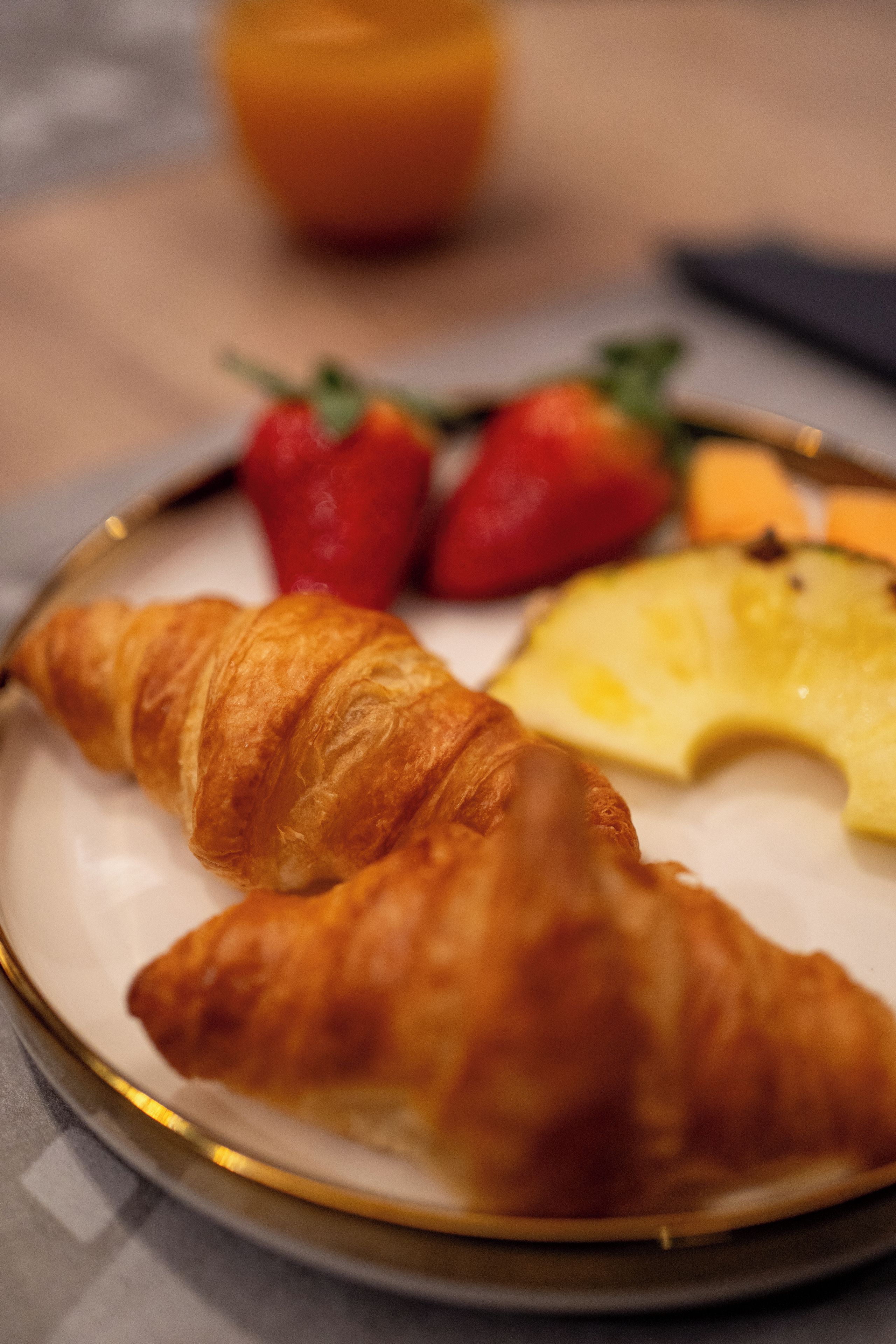A plate with two croissants, a slice of pineapple, and two strawberries.