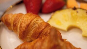 A plate with two croissants, a slice of pineapple, and two strawberries.