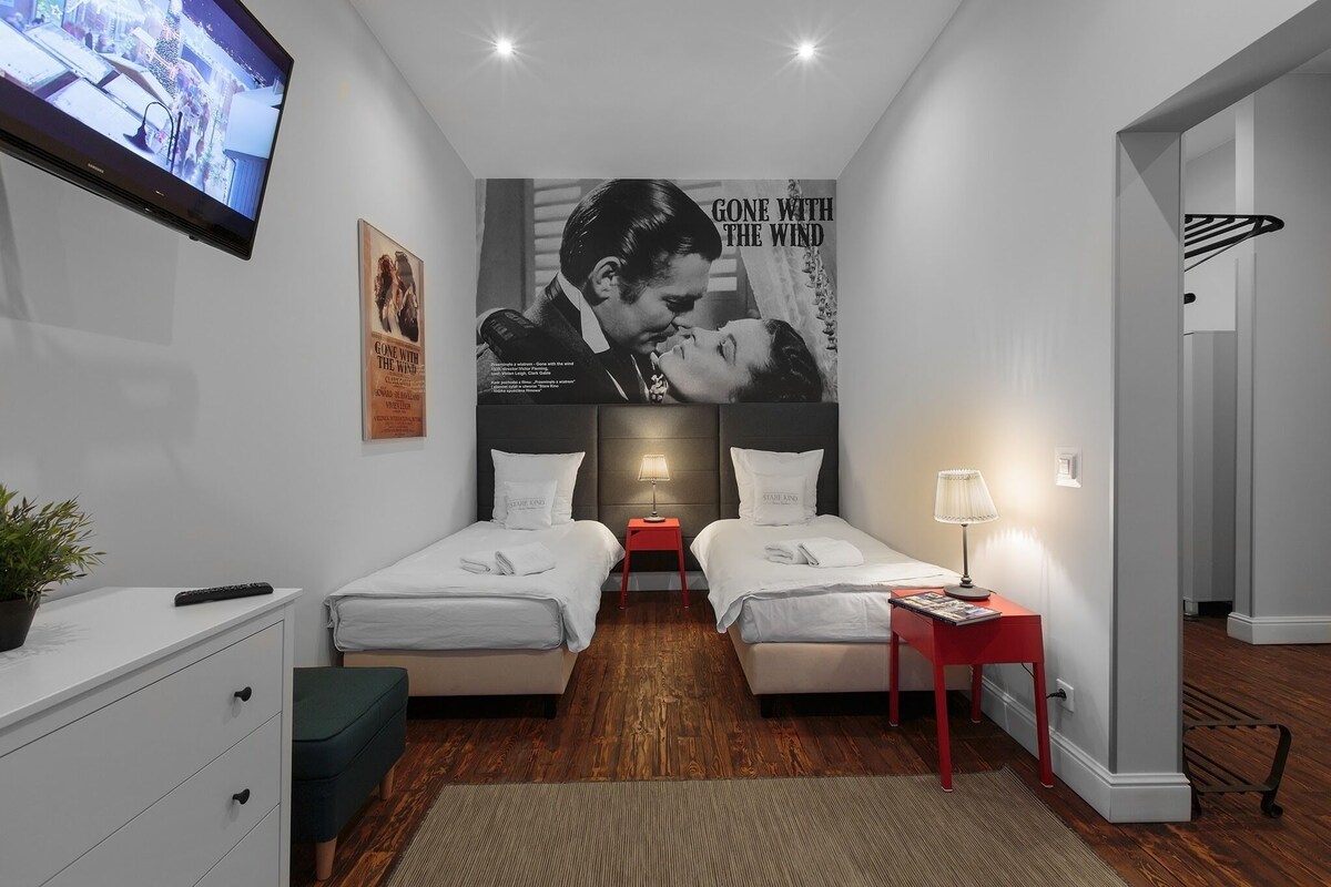 Ein Hotelzimmer mit zwei Betten, einem Fernseher, einem Plakat, einem Schreibtisch und einem Nachttisch in Rot.