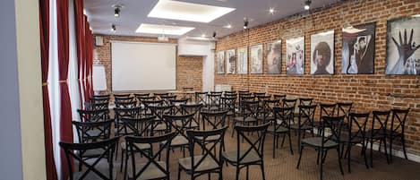 A conference room with rows of chairs, a whiteboard, and a brick wall with posters.
