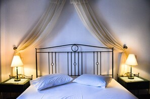 A bed with white linens, two bedside lamps, and a canopy with draped fabric. - Ifestia (Santorini)