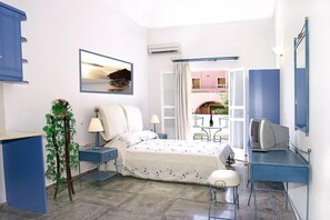 A bedroom with a bed, bedside tables, a desk, a chair, a TV, a window, and a balcony. - Ifestia (Santorini)