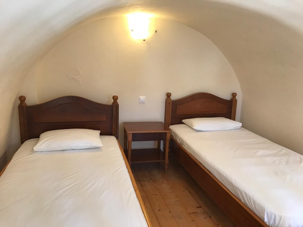 Ein kleines, gemütliches Zimmer mit zwei Holzbetten, einem Nachttisch und einer gewölbten Decke.