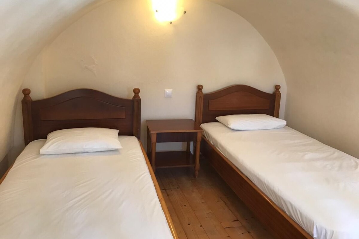A small, cozy room with two wooden beds, a nightstand, and a curved ceiling.