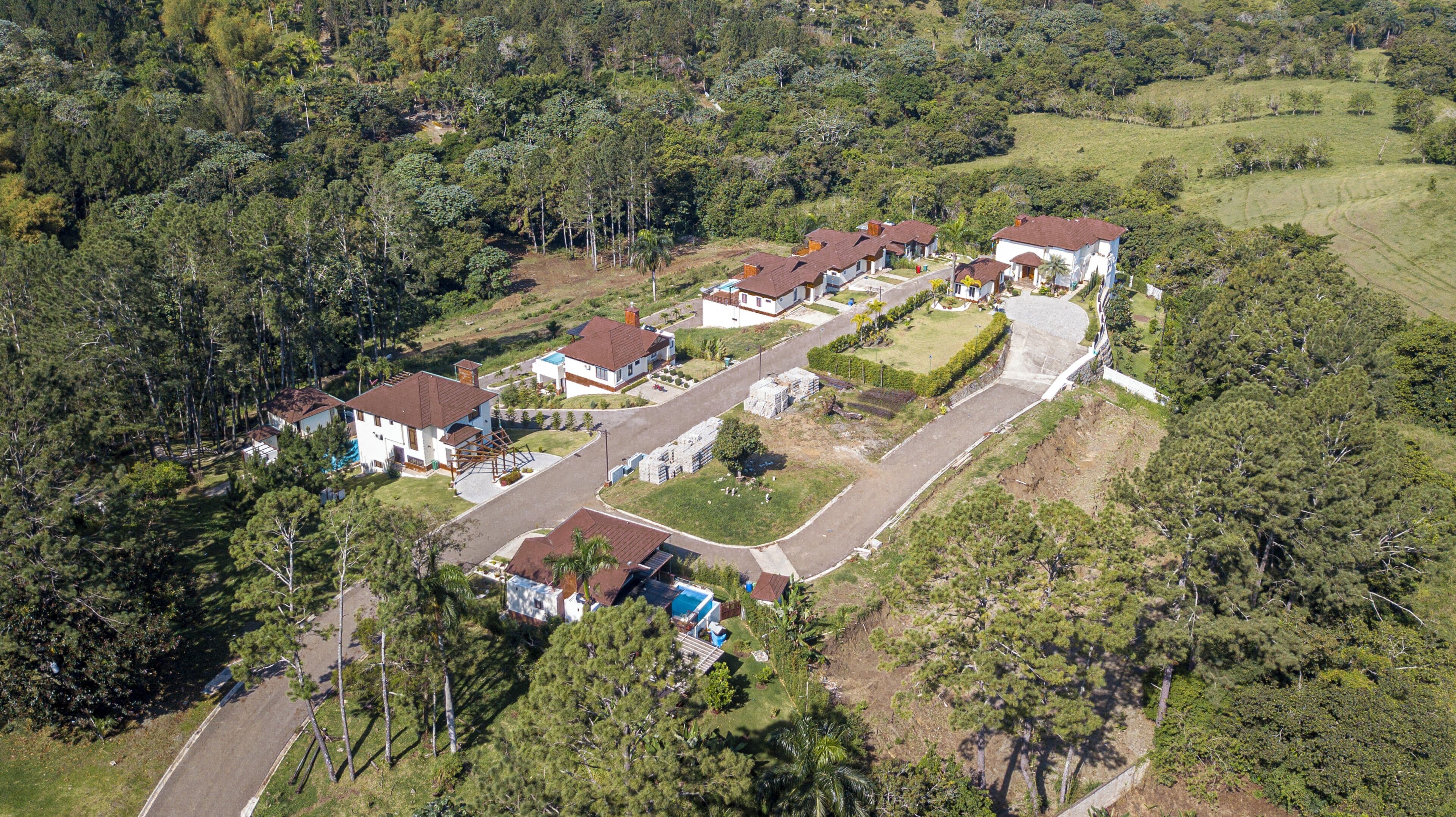 An aerial view of a residential area with houses, a road, and surrounding greenery.