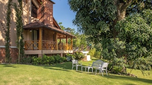 A building with a brick facade, a balcony with wooden railings, and a lawn with two white metal chairs. - Vista Del Campo Country Club & Villas Srl (Jarabacoa)