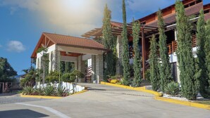 A modern building with a covered entrance, stone pillars, and a red-tiled roof. - Vista Del Campo Country Club & Villas Srl (Jarabacoa)