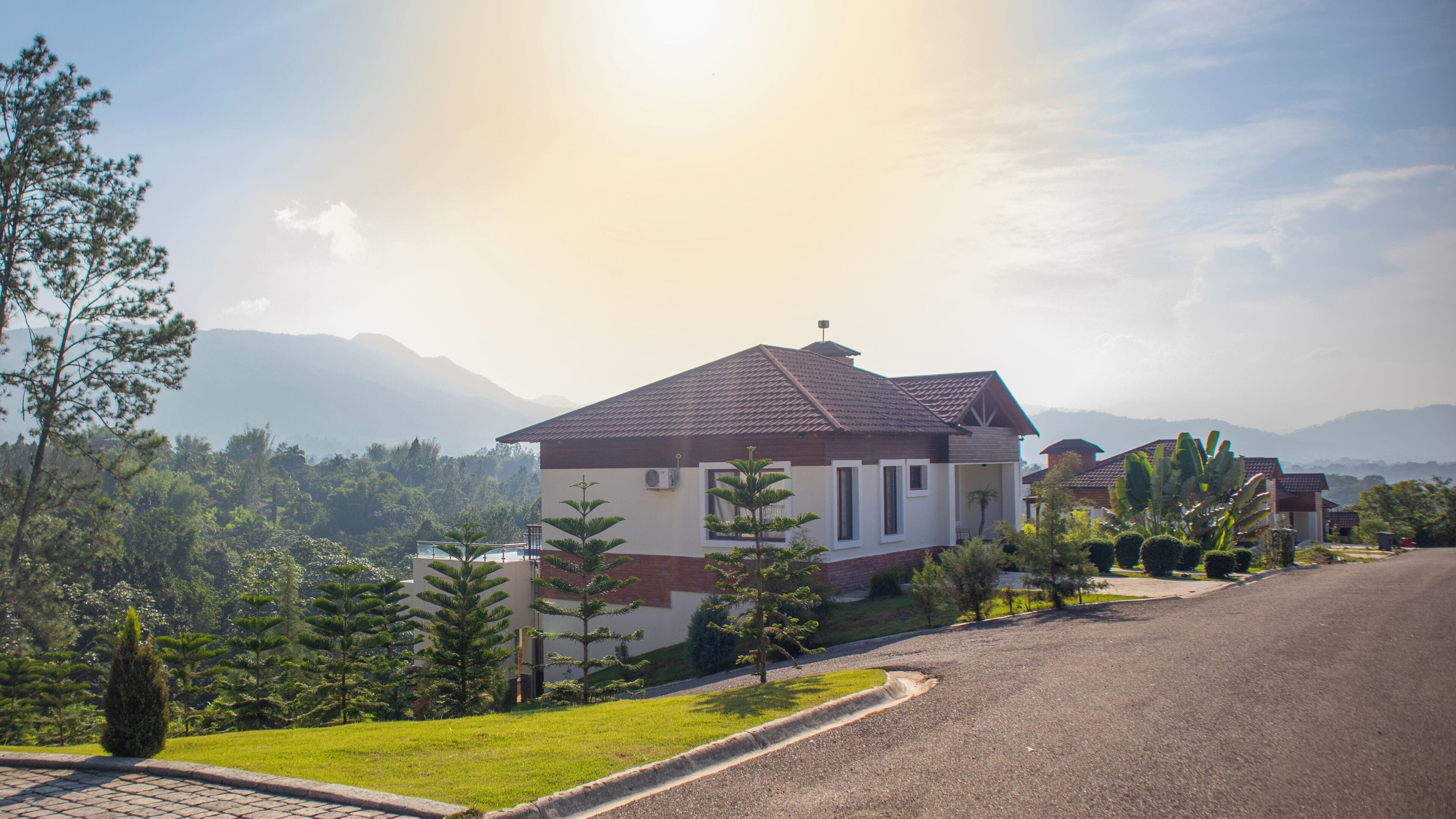 A residential area with houses, a paved road, and a mountainous backdrop.