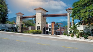 A gated entrance with a stone and brick structure, a clear sky, and a mountain in the background. - Vista Del Campo Country Club & Villas Srl (Jarabacoa)