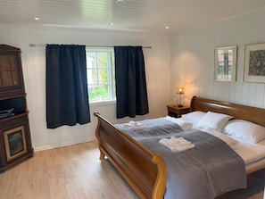 A bedroom with a wooden bed, a nightstand with a lamp, a window with curtains, and a cabinet. - Rjukan Hotel Admini (Tinn)