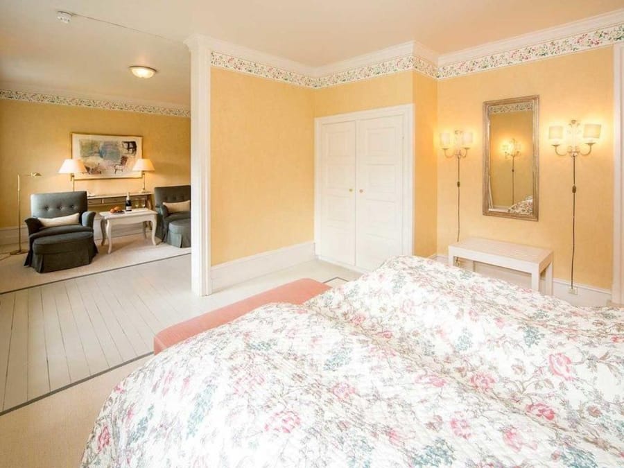 A bedroom with a bed, a desk, two chairs, a wardrobe, and a bathroom visible through an open door.