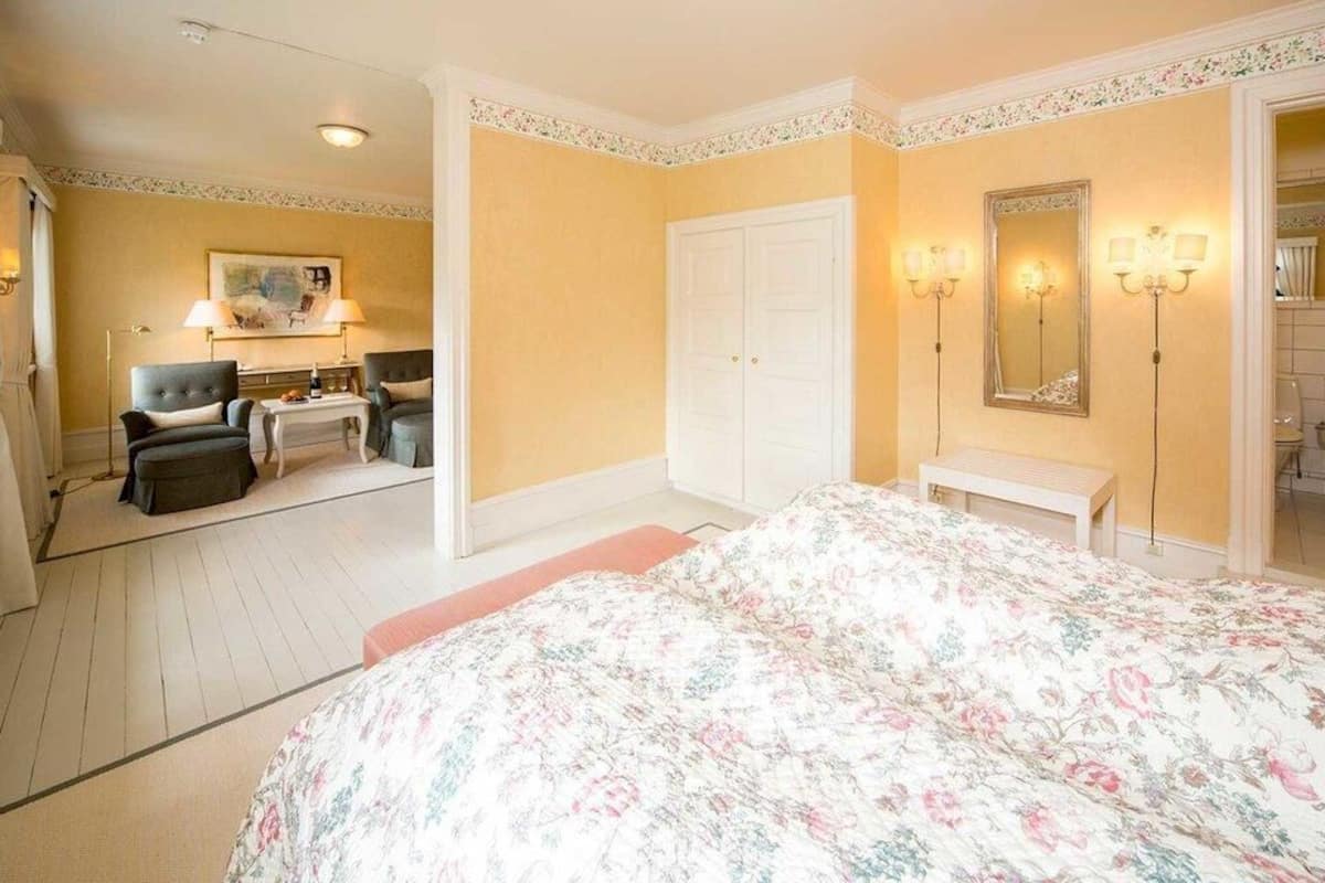 Ein Schlafzimmer mit Bett, Schreibtisch, zwei Stühlen, einem Kleiderschrank und einem durch eine offene Tür einsehbaren Badezimmer.