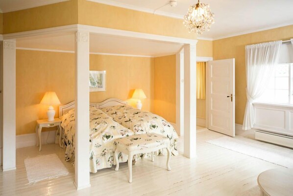 A bedroom with a four-poster bed, two bedside lamps, a chandelier, and a white door.